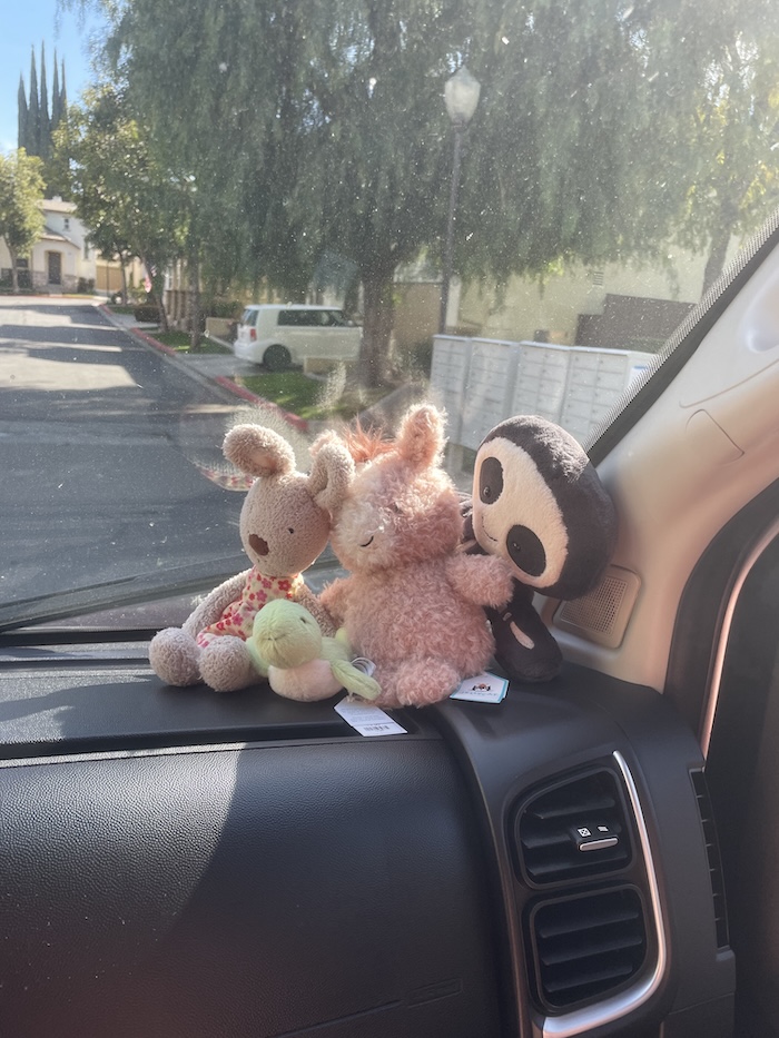 Three stuffed animals sitting on a van dashboard, facing the road ahead